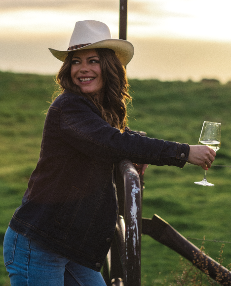 Jordan Wente leans on a fencepost with a glass of sauvignon black